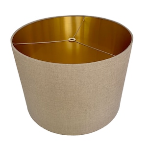 May include: A beige linen lampshade with a gold interior. The shade has a simple, cylindrical shape and is designed for use with a standard lamp base.
