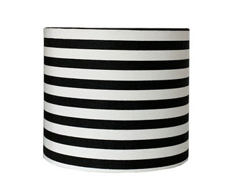 May include: Black and white striped lampshade. The lampshade is cylindrical and has a white fabric base with black horizontal stripes.