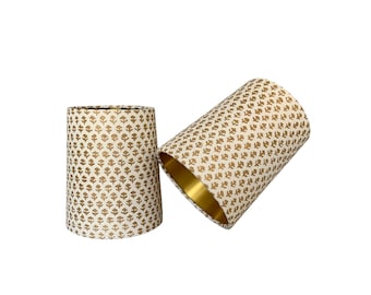 May include: Two white lampshades with a gold floral pattern. The lampshades are made of fabric and have a gold trim.