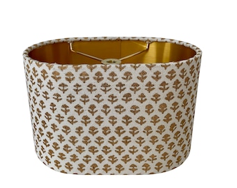May include: An oval lampshade with a white linen fabric exterior and a gold metallic interior. The fabric has a repeating pattern of small gold floral motifs.