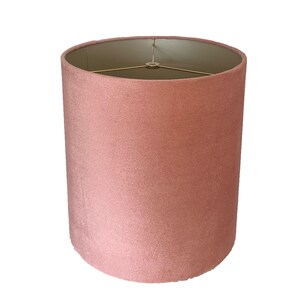 May include: A dusty rose pink lampshade made of velvet fabric. The lampshade has a gold metal frame.