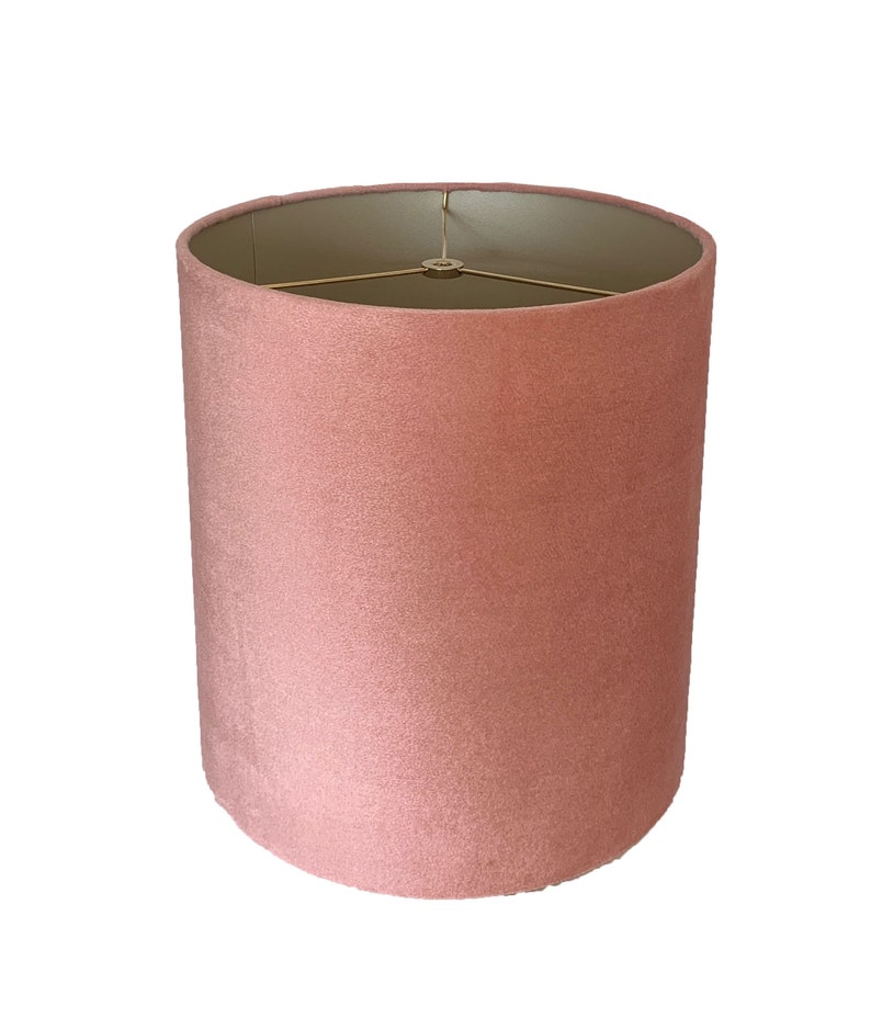 May include: A dusty rose pink lampshade made of velvet fabric. The lampshade has a gold metal frame.