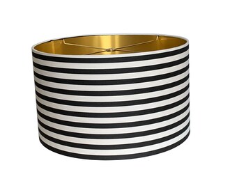 May include: Black and white striped lampshade with a gold interior. The lampshade is cylindrical in shape.
