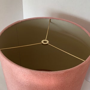 May include: A pink velvet lampshade with a gold metal frame. The lampshade is round and has a smooth texture.