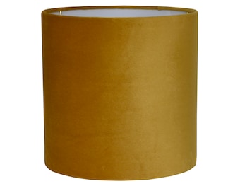 May include: A cylindrical lampshade made of a soft, mustard yellow velvet fabric.