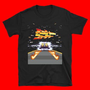 Puede incluir: Camiseta negra con un gráfico pixelado del DeLorean de Regreso al Futuro. El diseño incluye el logotipo de la película en rojo y amarillo, con llamas y efectos de relámpagos.