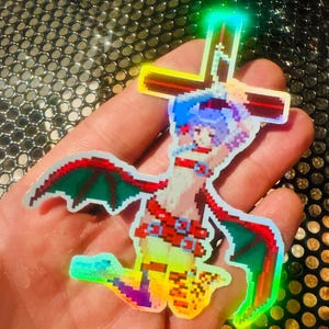 May include: Holographic sticker depicting a pixelated anime-style character with blue hair, a red collar, and wings, positioned under a cross. The sticker has a rainbow iridescent effect, with green, red, and yellow hues.