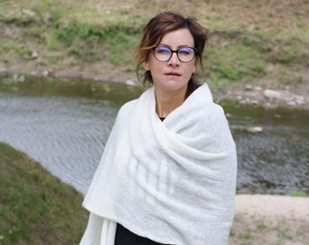 May include: A woman wearing a white knitted shawl over a black dress and black tights. She is wearing glasses and has brown hair.