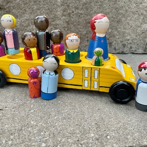 May include: A yellow school bus toy with a variety of painted wooden peg dolls, including a monkey, a girl with a blue shirt, a boy with a red shirt, a girl with a purple shirt, a boy with a green shirt, a girl with a blue shirt, a boy with a blue shirt, a girl with a red shirt, a boy with a brown shirt, and a girl with a red shirt.