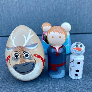 May include: A set of four hand-painted wooden figurines featuring characters from the film Frozen. The set includes a reindeer, a boy with brown hair, a girl with blonde hair, and Olaf the snowman. The figurines are painted in bright colours and have a whimsical style.