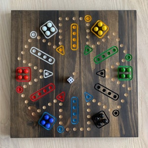 Peut inclure: Un plateau de jeu en bois avec un fond brun et une variété de cercles et de carrés colorés. Le plateau est conçu pour un jeu de Ludo, un jeu de société populaire.