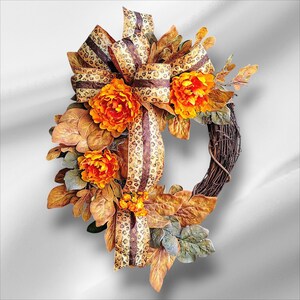 May include: A fall-themed wreath with a brown grapevine base. It features orange and yellow flowers, brown and tan leaves, and a large bow with a leopard print pattern. The wreath is designed for seasonal home decor.