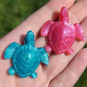 May include: Two small resin turtle figurines, one is teal blue and the other is pink with iridescent glitter.