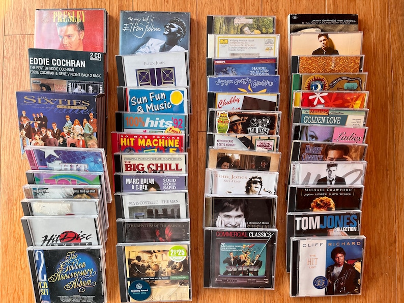 May include: A collection of music CDs arranged in four vertical columns. The cases feature various artists and titles including Elvis Presley, Elton John, Eddie Cochran, The Big Chill, Tom Jones, and Cliff Richard, with diverse graphic designs.