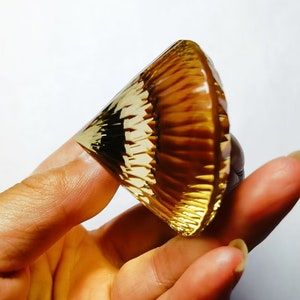 May include: A golden yellow, faceted, cone-shaped crystal with a striated pattern.