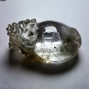 以下が含まれることがあります： 透明な水晶が、龍の形に彫刻されています。龍は横向きに寝ていて、頭は右を向いています。水晶は透き通っていて、わずかに緑がかった色をしています。
