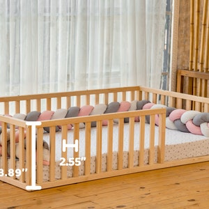 May include: A wooden playpen with a padded, braided bumper in pink, gray, and white. The playpen measures 18.89 inches wide and 2.55 inches high.