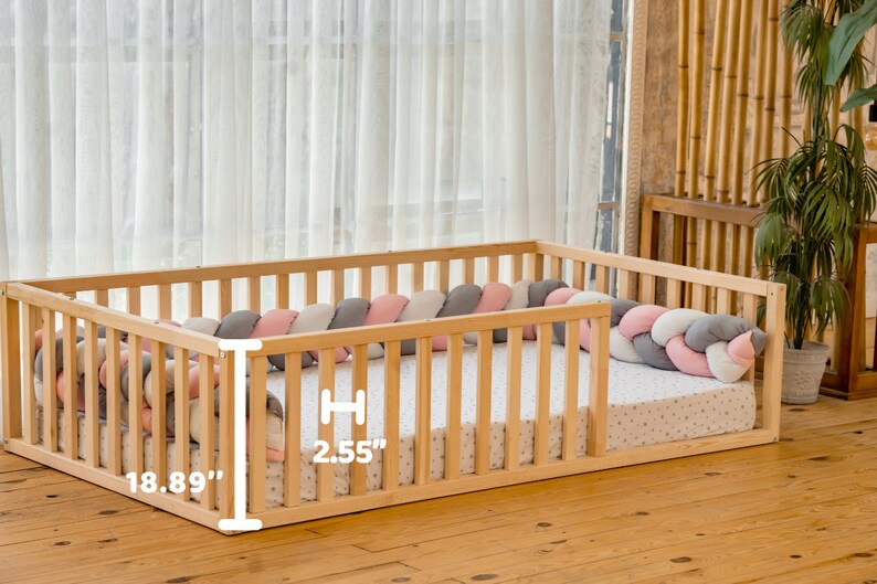May include: A wooden playpen with a padded, braided bumper in pink, gray, and white. The playpen measures 18.89 inches wide and 2.55 inches high.