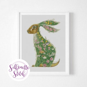 May include: A cross-stitch pattern of a green rabbit with flowers and leaves. The rabbit is sitting on its haunches with its ears up. The background is white.