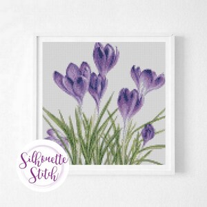 May include: Cross stitch pattern featuring a bouquet of purple crocuses with green leaves. The pattern is framed in a white frame.