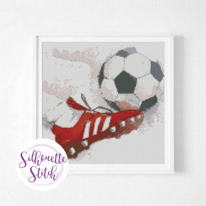 May include: A red and white soccer cleat kicking a black and white soccer ball. The image is pixelated, giving it a cross-stitch appearance.