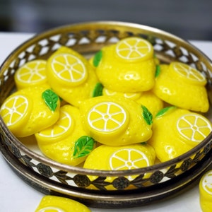 May include: A silver tray filled with yellow lemon-shaped buttons with green leaves. The buttons have white centers with a lemon slice design.