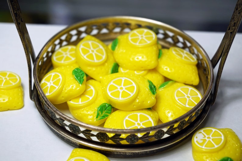 May include: A silver tray filled with yellow lemon-shaped buttons with green leaves. The buttons have white centers with a lemon slice design.