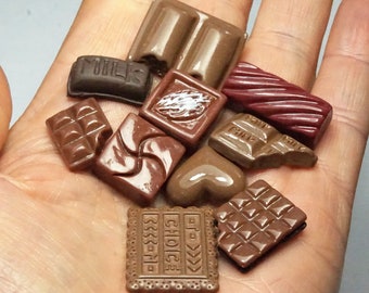 May include: A collection of miniature chocolate bars, including milk chocolate, dark chocolate, and white chocolate. Some of the bars have embossed designs, such as "Milk" and "Choice".