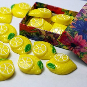 May include: A box of yellow lemon-shaped buttons with green leaves. The box is open and has a floral pattern.