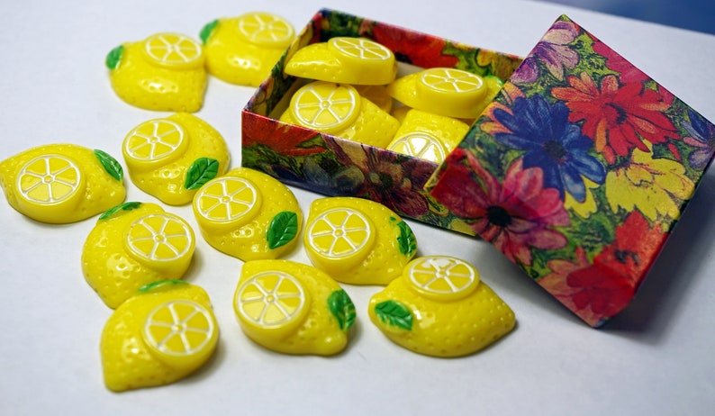 May include: A box of yellow lemon-shaped buttons with green leaves. The box is open and has a floral pattern.