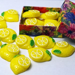 May include: A box of yellow lemon-shaped resin cabochons with green leaves. The box is decorated with a floral pattern.