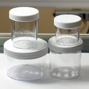 Peut inclure: Trois bocaux en plastique transparent avec des couvercles blancs. Les bocaux sont de tailles différentes et sont disposés en rangée du plus grand au plus petit.