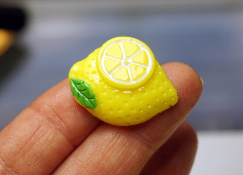 May include: A yellow lemon charm with a green leaf and a white lemon slice on top. The charm is made of polymer clay and is about 2 inches long.