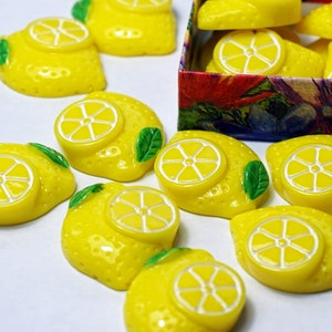 May include: A collection of yellow lemon-shaped buttons with green leaves. The buttons have a white center with a lemon slice design.