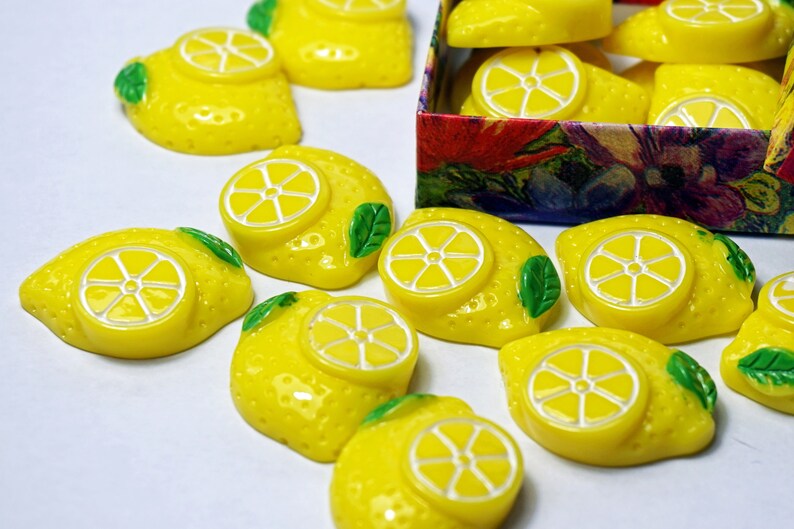 May include: A collection of yellow lemon-shaped buttons with green leaves. The buttons have a white center with a lemon slice design.