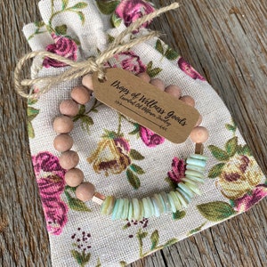 May include: A wooden and shell beaded bracelet with a copper accent. The bracelet is in a small floral fabric bag with a tag that reads "Drops of Wellness Goods Essential Oil Diffuser Jewelry".