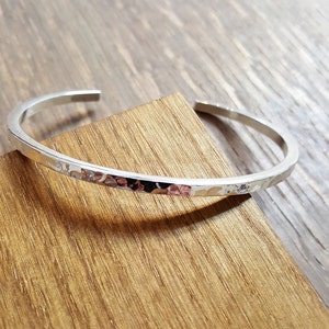 May include: A silver hammered bangle bracelet with a slightly rounded shape.