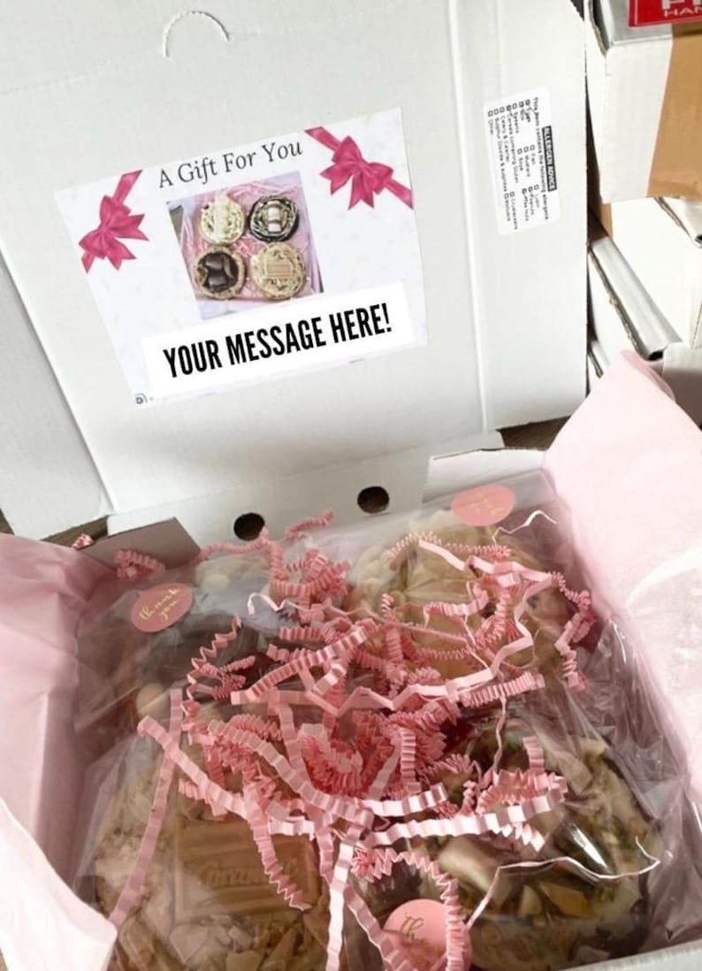 May include: A white cardboard gift box containing individually wrapped cookies nestled in pink shredded paper. The inside lid features a label with pink bows, the text A Gift For You, and a placeholder box labeled YOUR MESSAGE HERE!