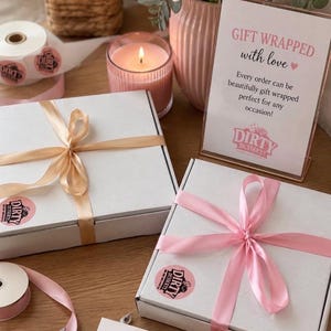 May include: Two square white cardboard boxes tied with satin ribbons, one in champagne and one in light pink. Each box features a round pink sticker with the text Dirty Desserts. A sign reads GIFT WRAPPED with love and Dirty Desserts.