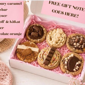 May include: A white gift box containing six assorted cookies topped with various chocolate candies. The box includes pink tissue paper and a sign that reads FREE GIFT NOTE GOES HERE! The text lists Cadbury caramel, Milkybar, Malteser, Biscoff & Kitkat, Kinder, and Chocolate orange.
