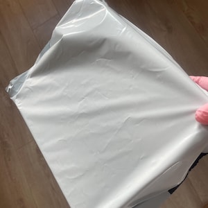 May include: A rectangular shipping mailer bag made of smooth, opaque white plastic material. The bag features a sealed top edge and a flexible, lightweight construction with visible creases across the surface from handling and storage.