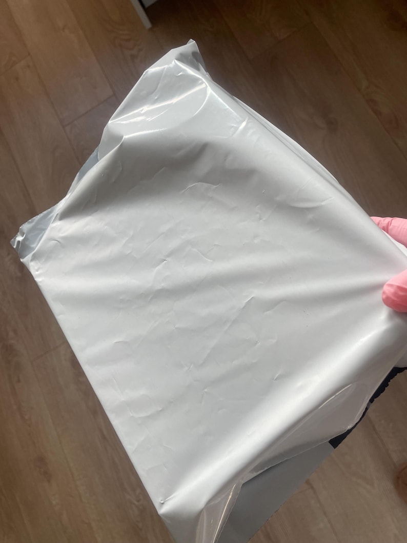 May include: A rectangular shipping mailer bag made of smooth, opaque white plastic material. The bag features a sealed top edge and a flexible, lightweight construction with visible creases across the surface from handling and storage.