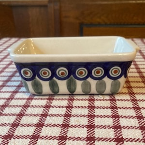 Puede incluir: Un pequeño molde para hornear de cerámica blanca con diseños florales azules y verdes. El molde tiene forma rectangular y dos pequeñas asas a los lados.