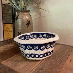May include: A blue and white ceramic bowl with a geometric design. The bowl has a white rim and a blue and white pattern of circles and lines. The bowl is sitting on a wooden surface.