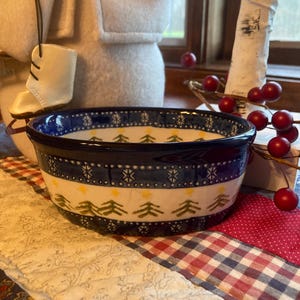 Könnte beinhalten: Eine blaue und weiße Keramikschüssel mit einem winterlichen Design mit grünen Tannenbäumen und Schneeflocken. Die Schüssel ist mit einem gelben Band und goldenen Sternen verziert.