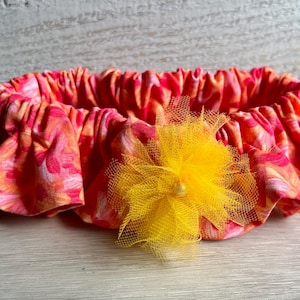May include: A pink and orange fabric headband with a yellow tulle flower.