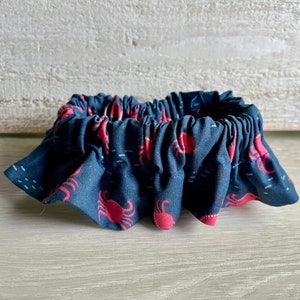 May include: A blue and red fabric ruffle with a crab pattern. The ruffle is gathered and has a ruffled edge.