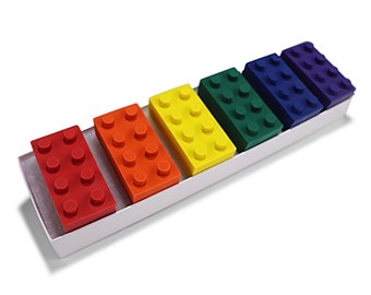 May include: A set of six crayons shaped like colorful Lego bricks. The crayons are arranged in a rainbow order from red to purple. The crayons are in a white box.