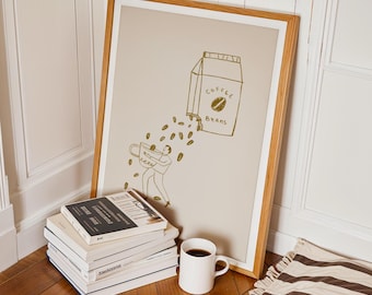 May include: A framed illustration of a person pouring coffee beans from a box labeled "Coffee Beans" into a cup. The illustration is in gold on a beige background. A white coffee mug sits on a wooden floor in front of the framed illustration.