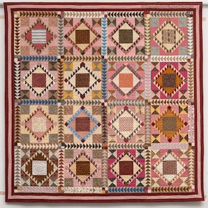 May include: A quilt with a patchwork design featuring a variety of colors and patterns, including pink, brown, and white. The quilt is made up of 16 squares, each with a different design. The quilt is framed with a red border.